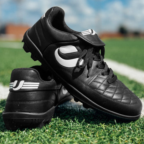 Pair of Umpiro Pro black referee shoes on an artificial pitch