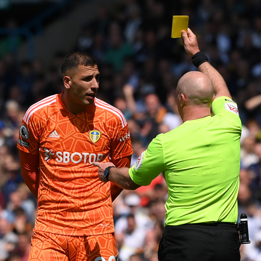 Referee in a green kit showing a yellow card to a player