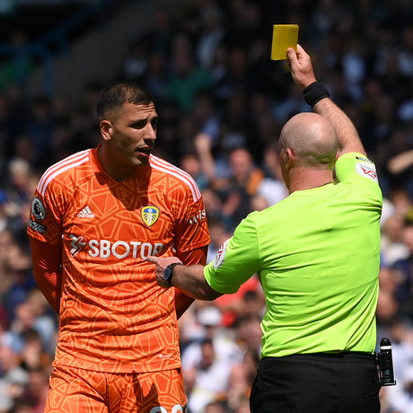 Referee in a green kit showing a yellow card to a player